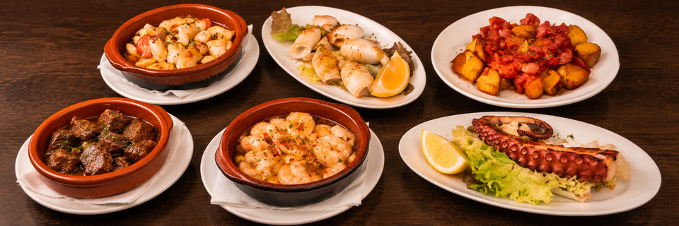 Tapas mit Gambas, Pulpo und Kartoffeln auf dem dunklen Restauranttisch
